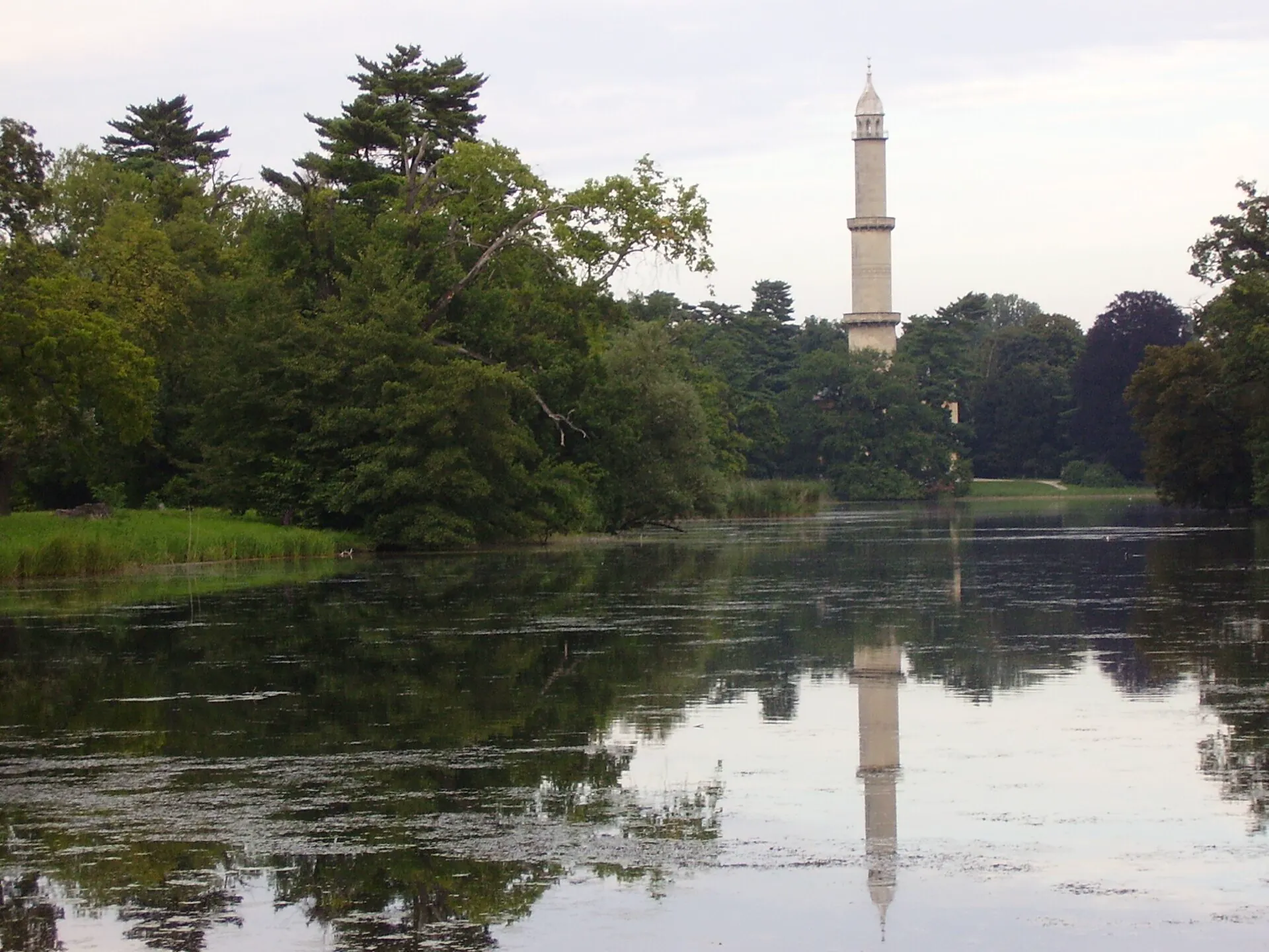 Věž minaretu odrážející se v hladině rybníka v zámeckém parku