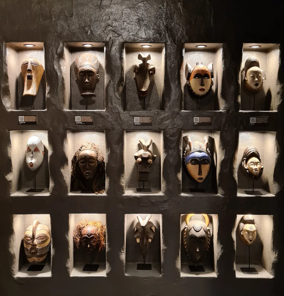 Stěna s patnácti nasvícenými africkými maskami