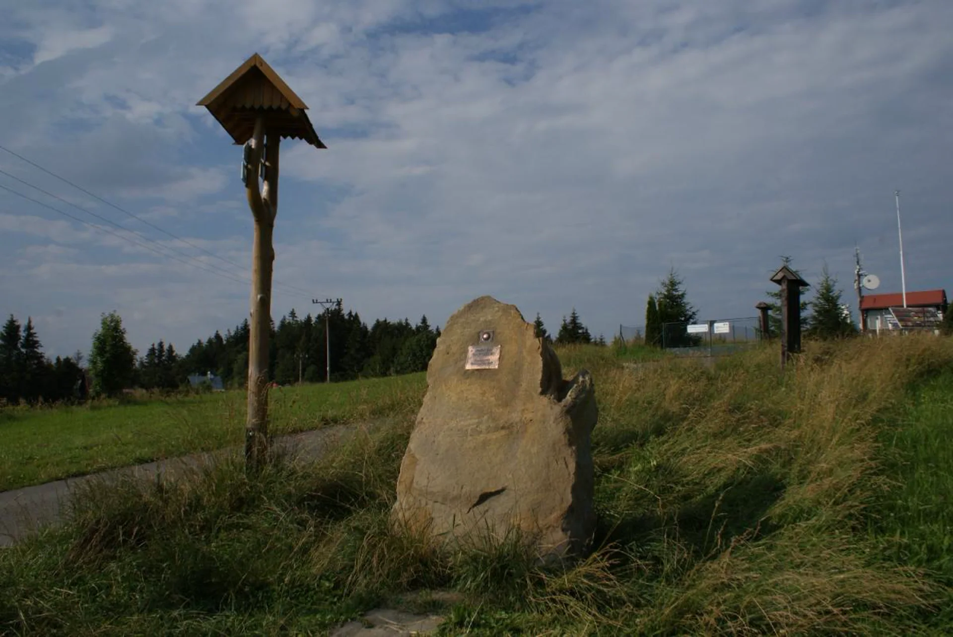 Dřevěný kříž se stříškou a kamenný hladicí bod u asfaltové cesty na vrcholu Maruška