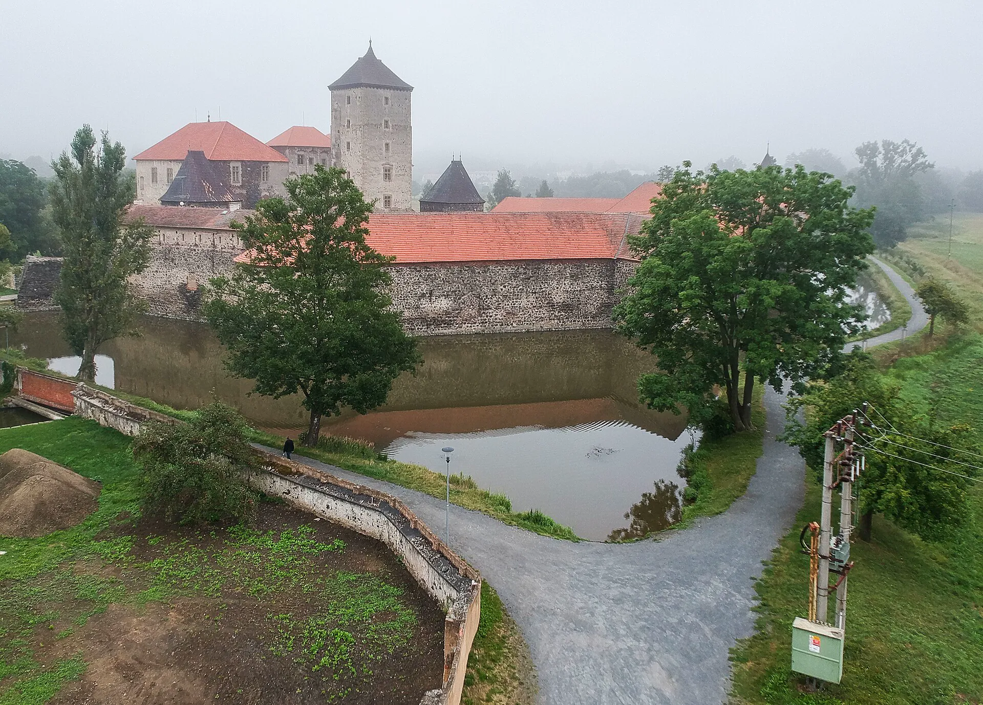 Pohled shora na hrad obklopený vodním příkopem v mlze