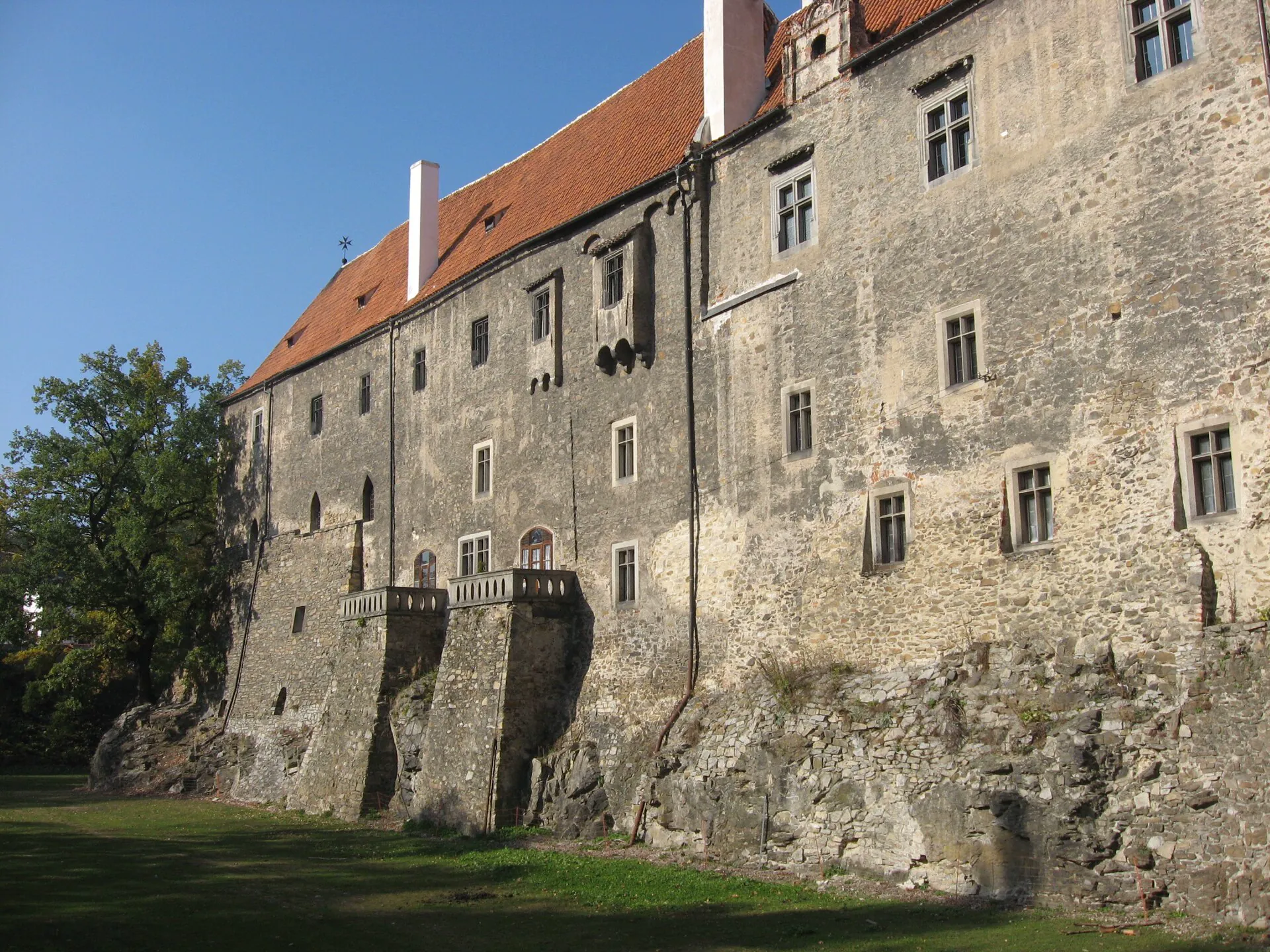 Dlouhé průčelí hradního paláce s opěrnými pilíři nad trávníkem