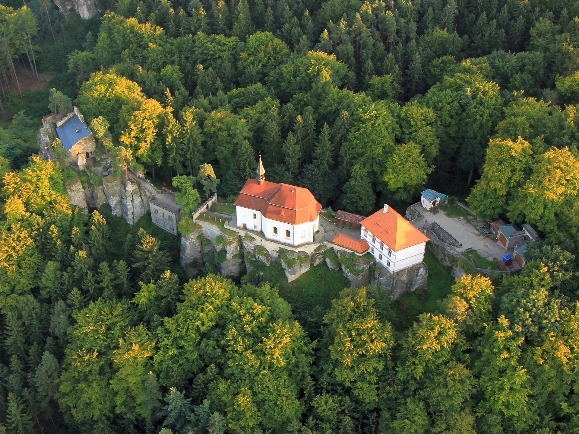 Letecký pohled na hrad Valdštejn s kaplí a červenými střechami mezi lesy