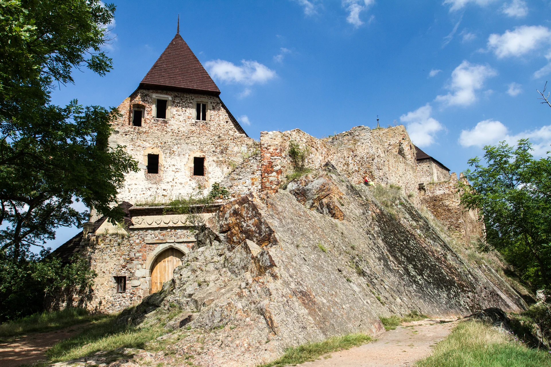 Hranolová věž hradu Točník nad zbytky kamenných hradeb, letní obloha s mraky