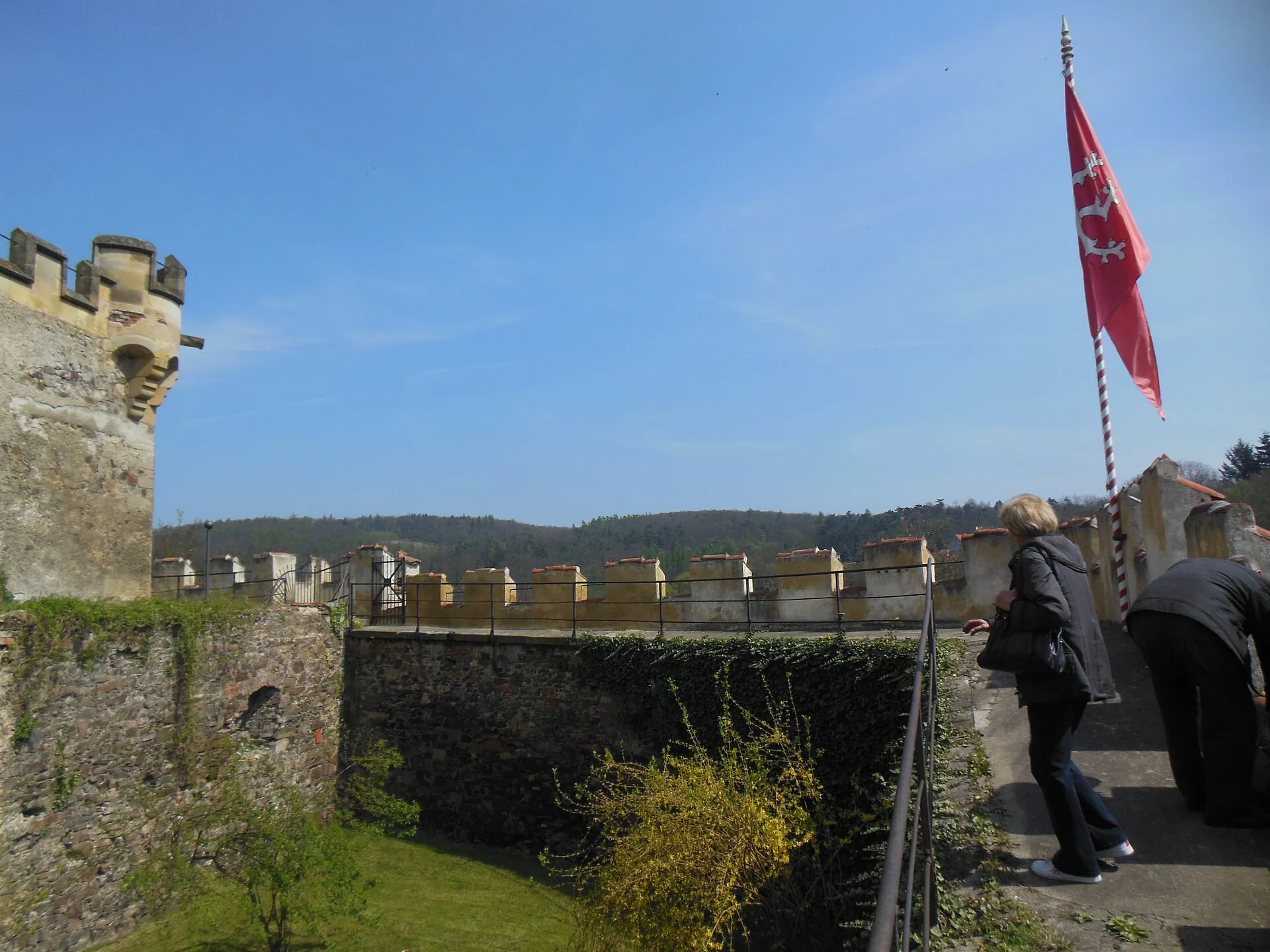 Hradby s cimbuřím a vlajkou nad zeleným příkopem