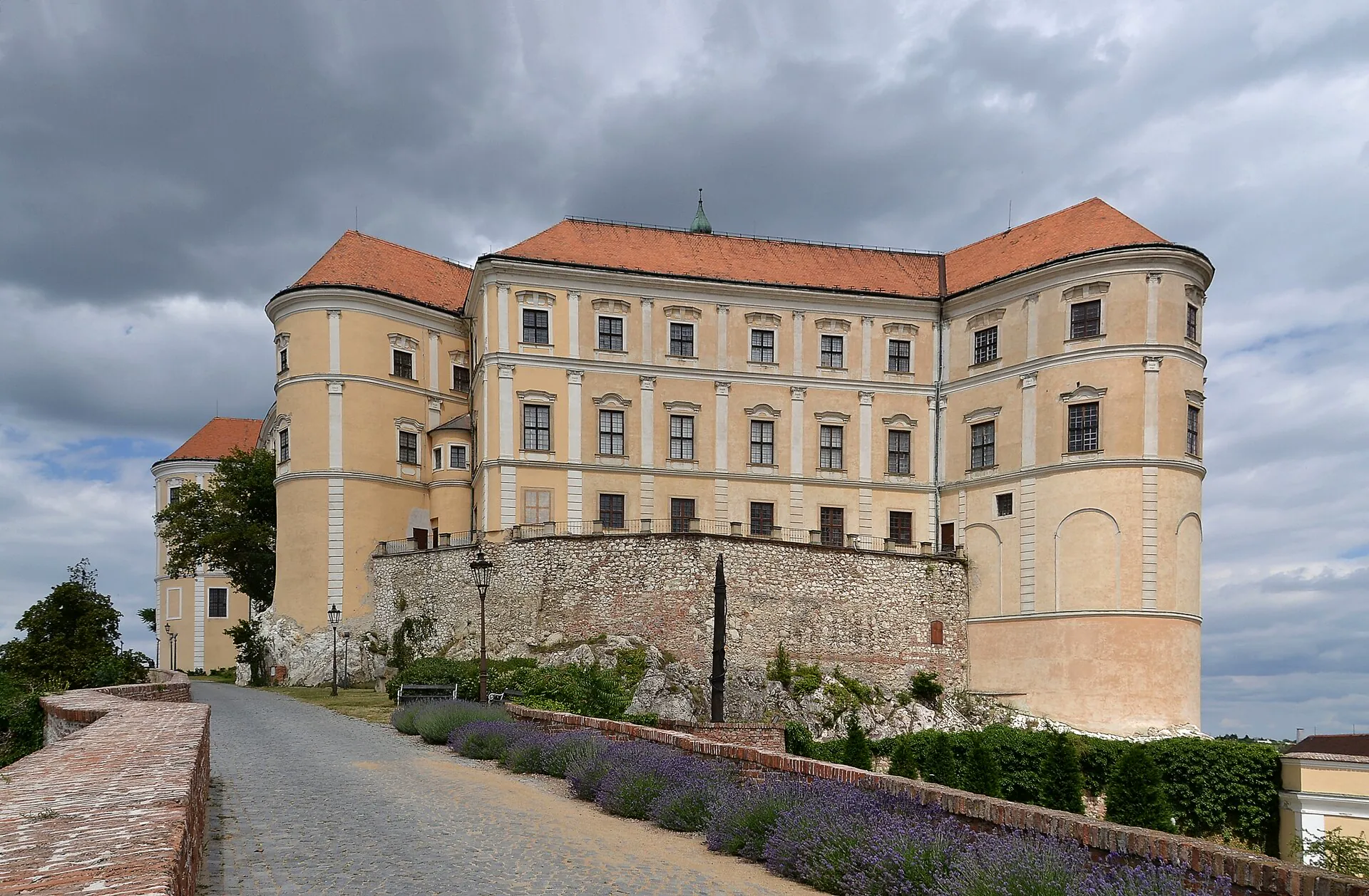 Průčelí zámku s levandulovým záhonem pod bouřkovou oblohou