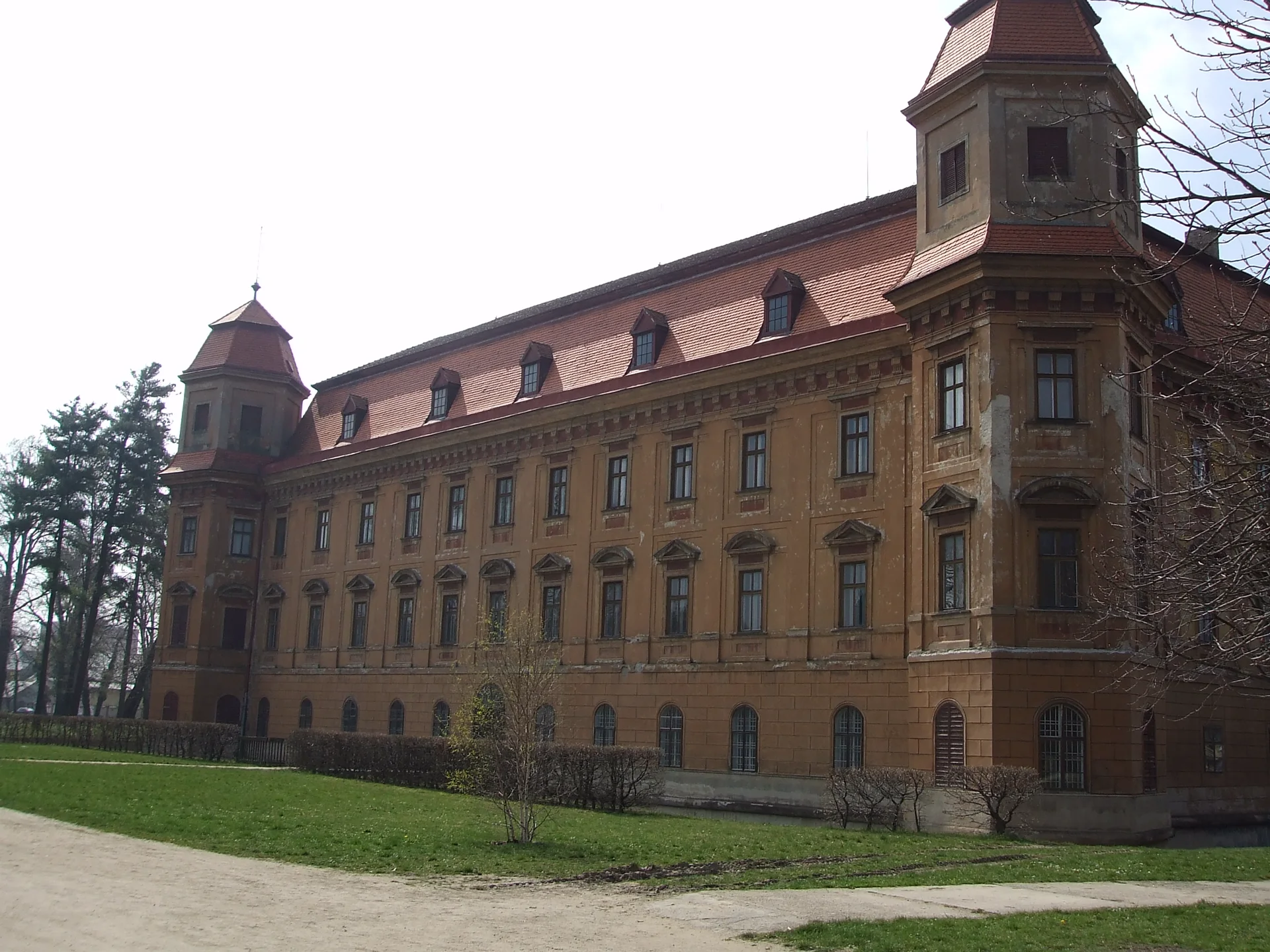 Boční průčelí zámku Holešov s okrovou fasádou a věžemi, pohled z parku