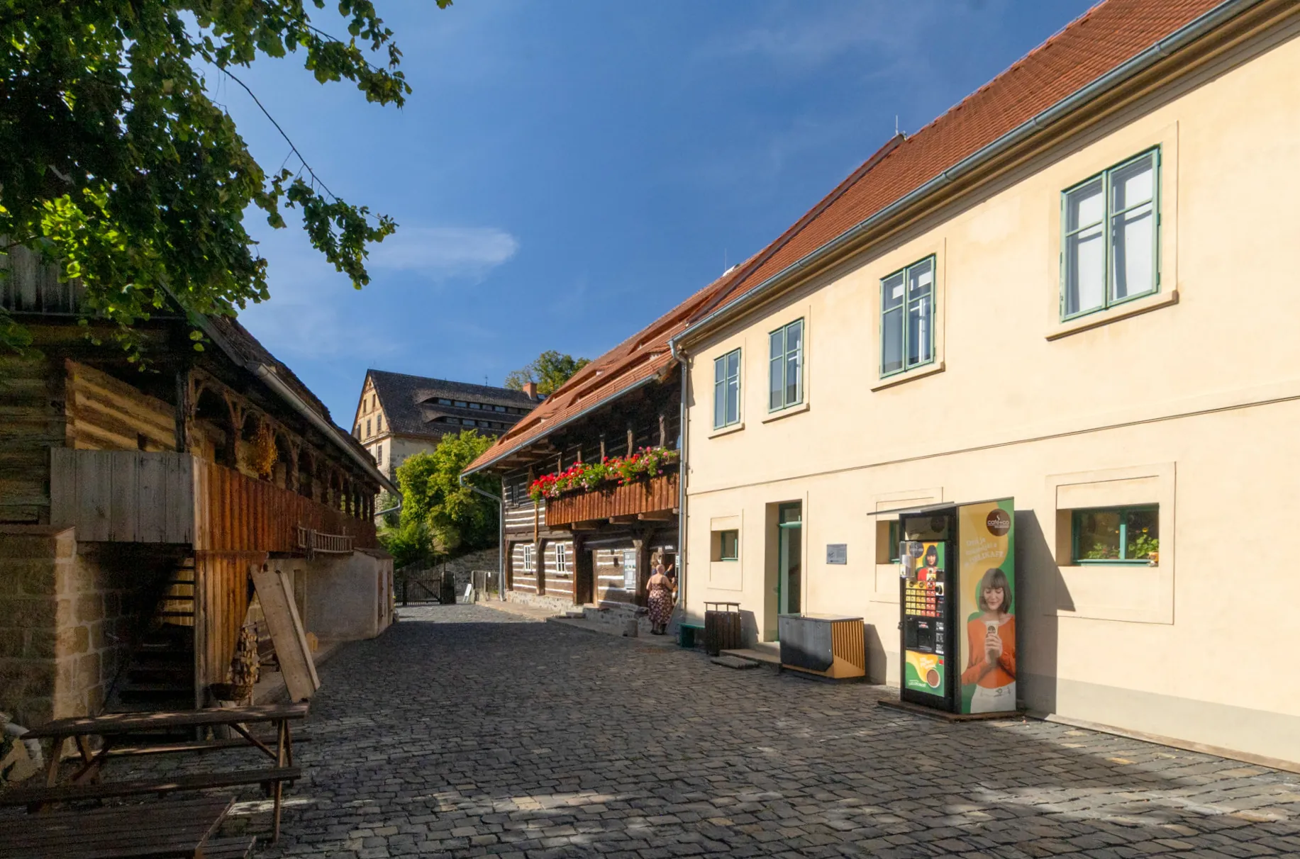 Prosluněná vesnická ulička s obchodem a roubenými staveními