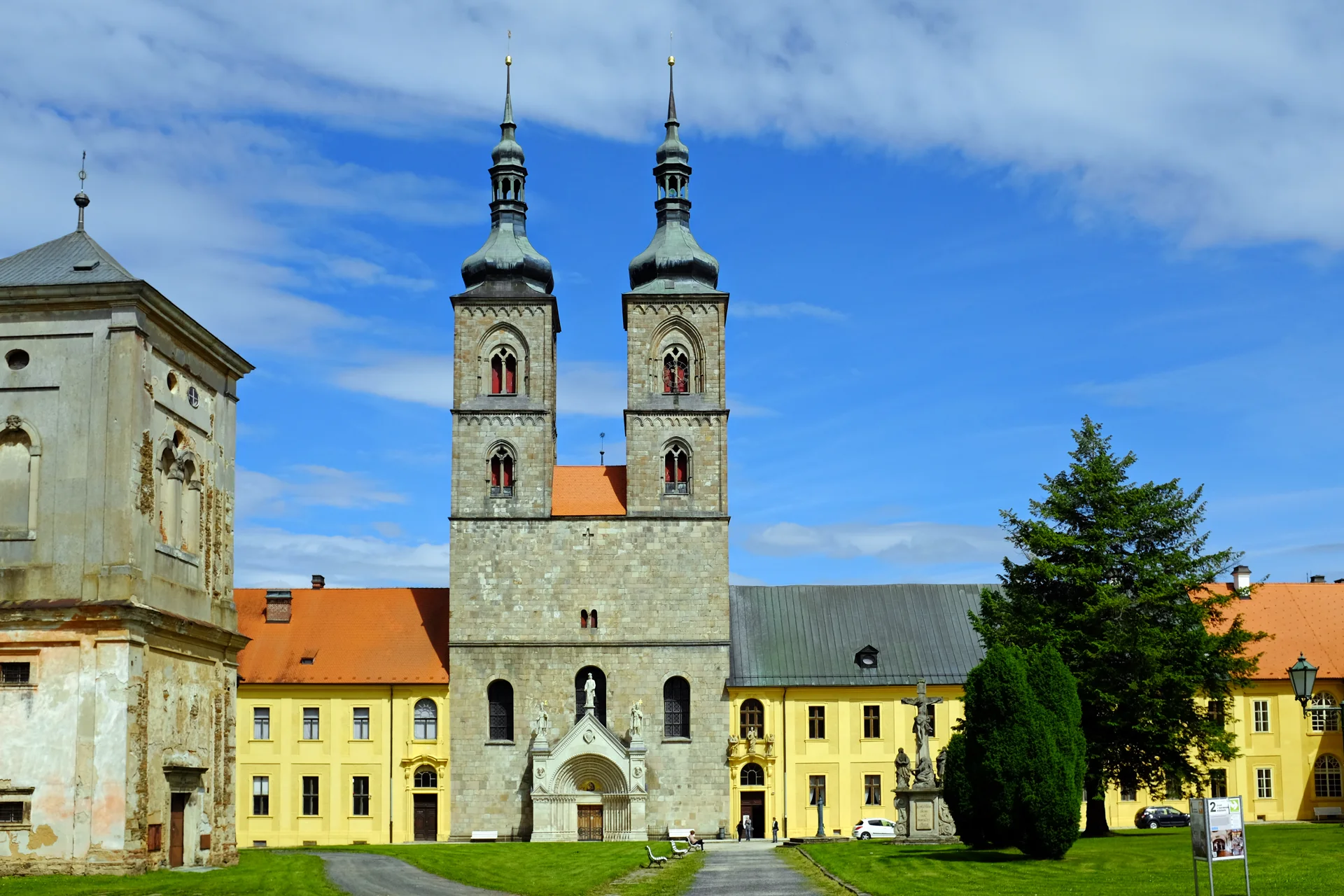 Klášter Teplá s dvouvěžovým kostelem a žlutými budovami konventu v letní zeleni