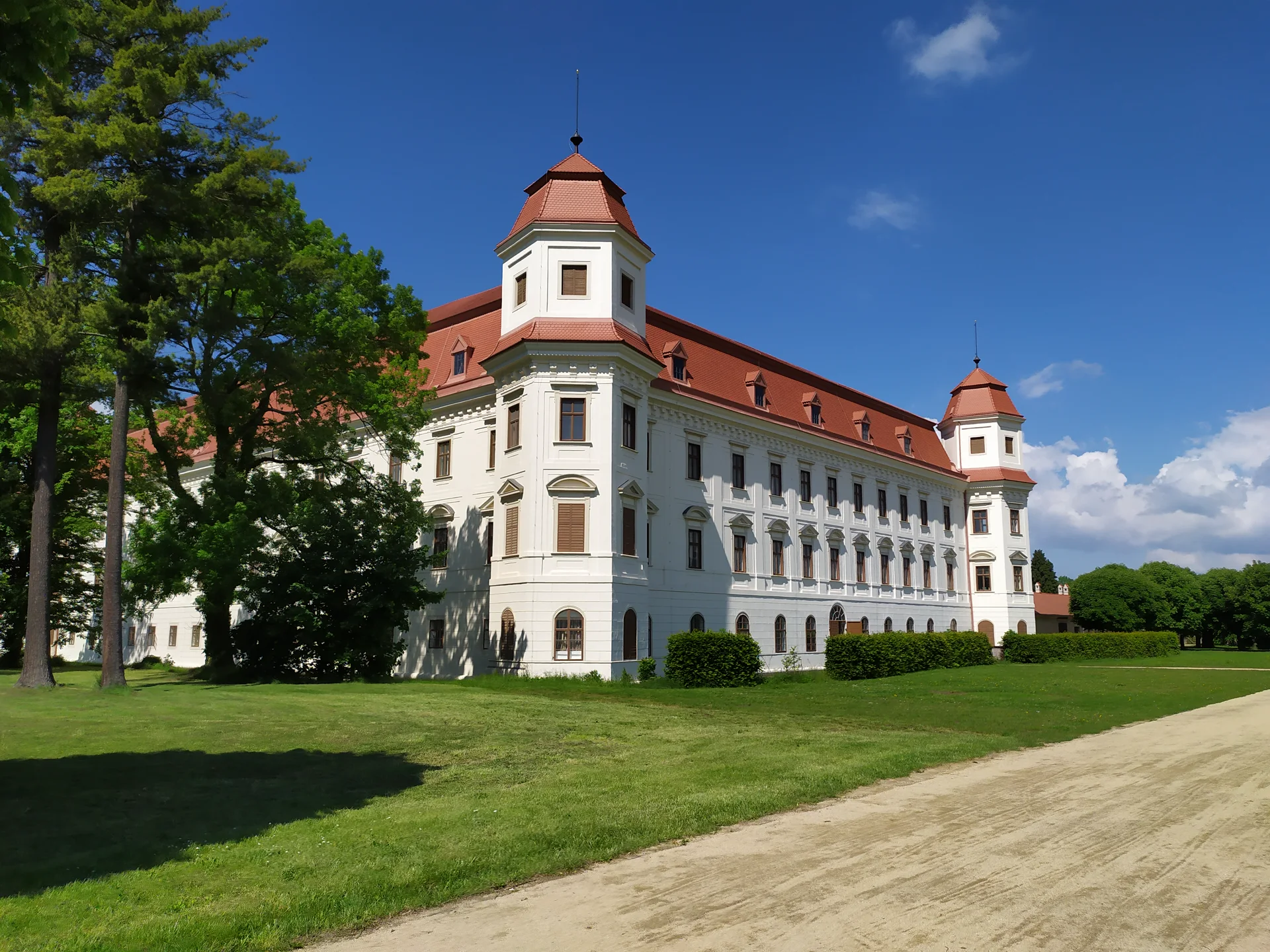 Bílá barokní budova zámku Holešov s věžemi, pohled ze zámecké zahrady