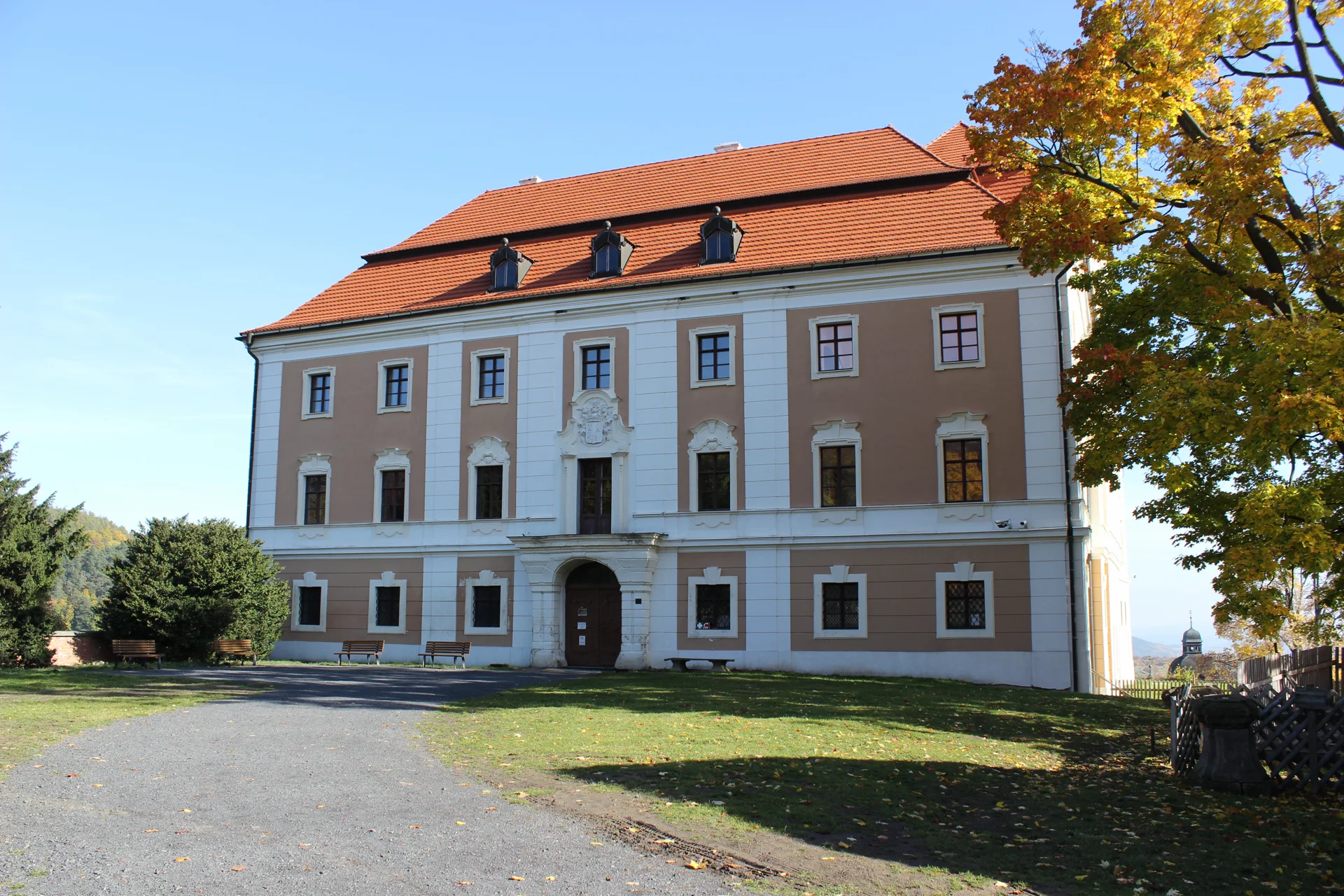 Dvoupatrová zámecká budova s mansardovou střechou, vikýři a znakem nad vstupním portálem