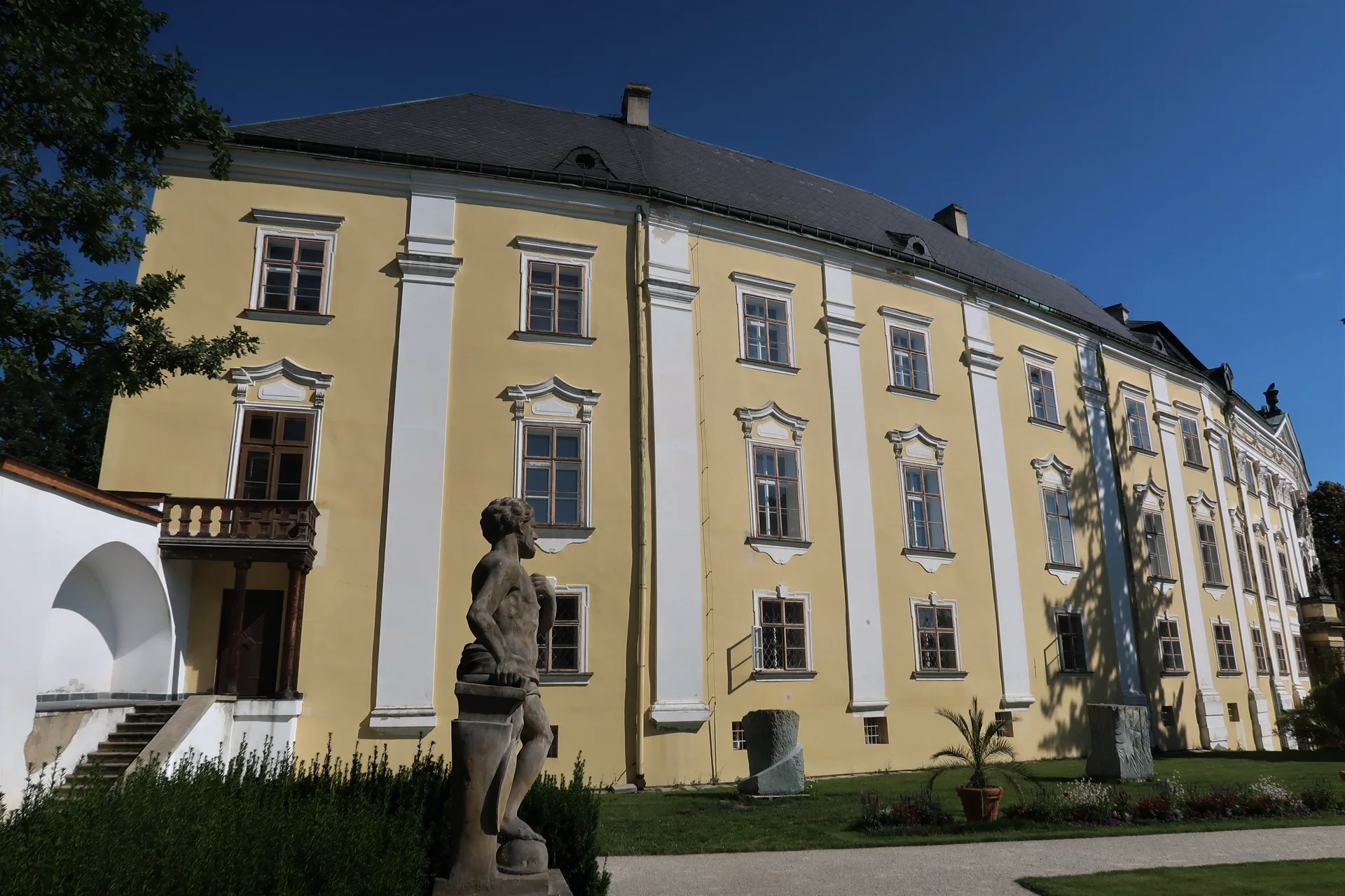 Žlutobílá fasáda zámku v Bruntále od zahrady, v popředí kamenná socha