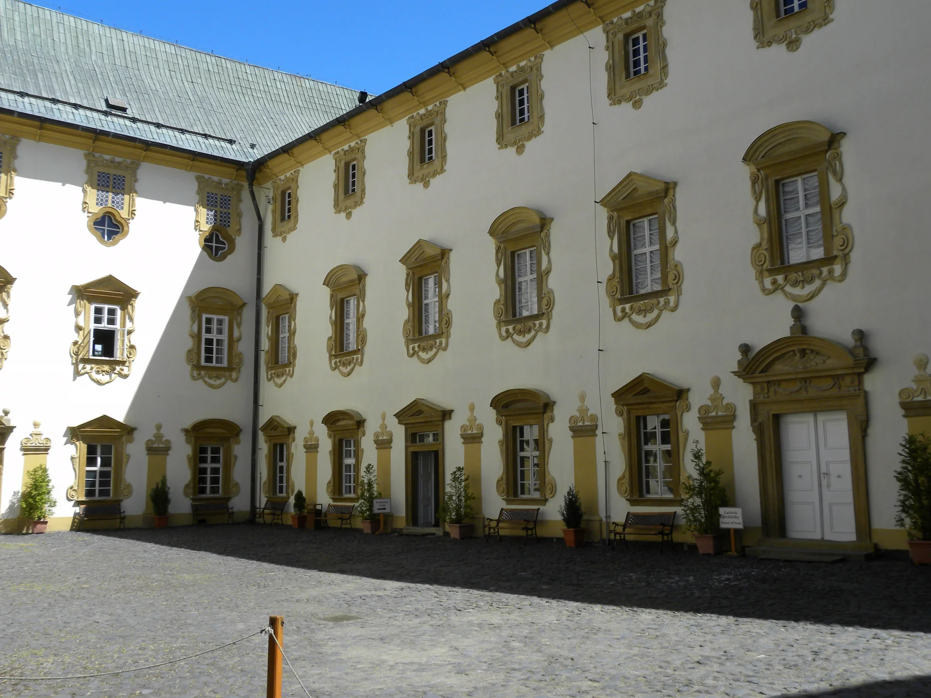 Nádvoří zámku Lemberk se světlou barokní fasádou, kamennými portály a řadami zdobených oken