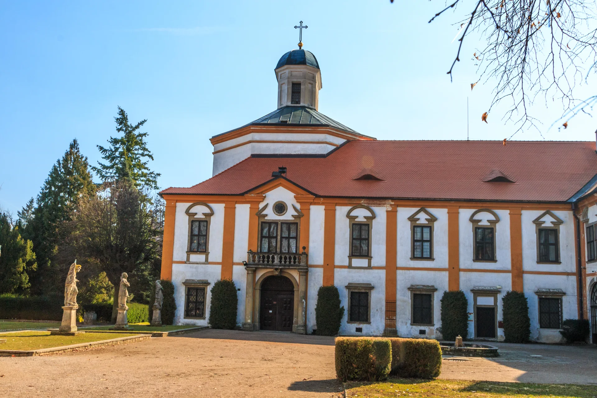 Hlavní průčelí zámku Choltice s kaplí a bání, před ním nádvoří se sochami a tvarovanými keři