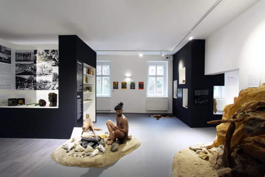 Figurína pravěkého lovce u ohniště v expozici s kamennou scenérií