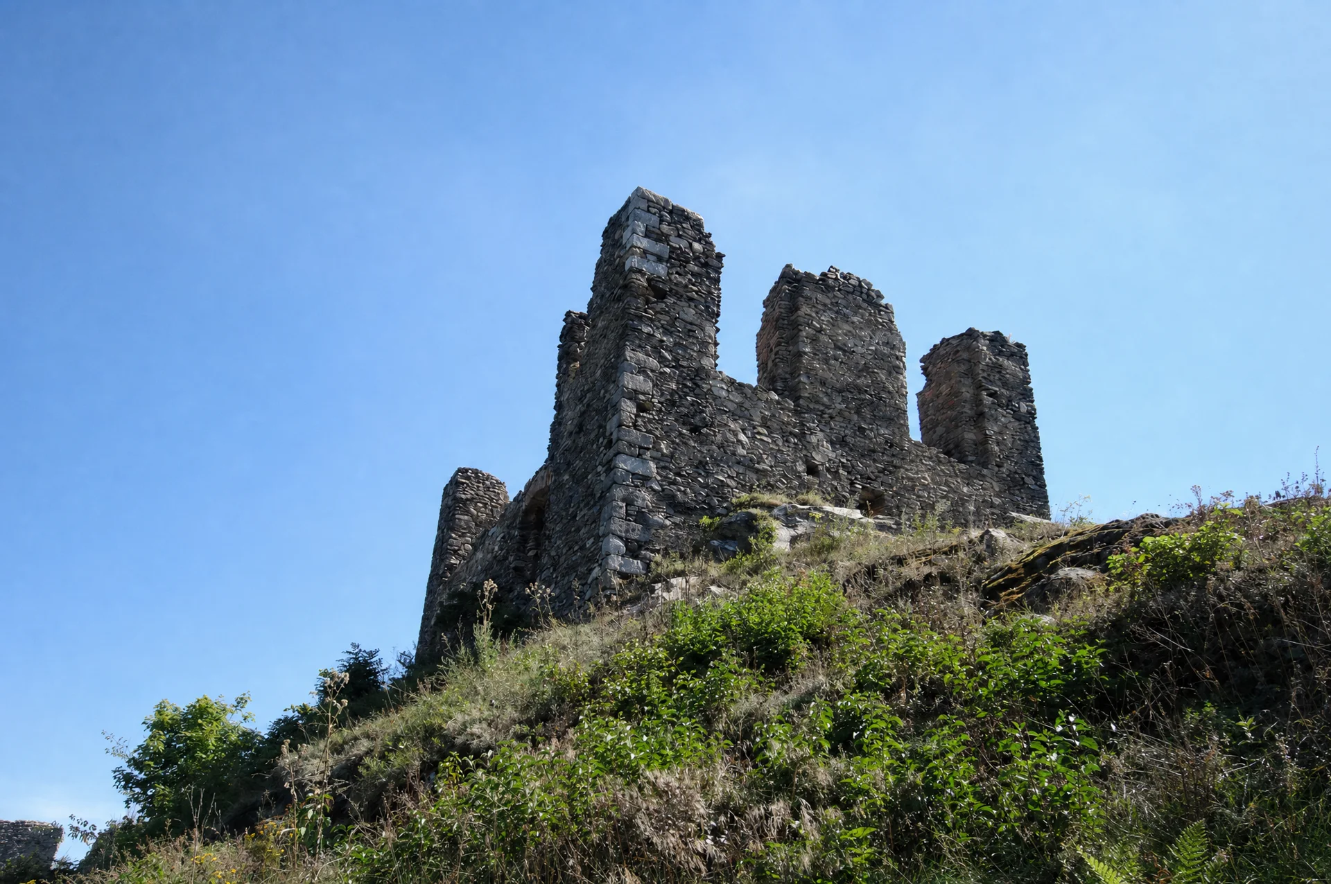 Tři stojící fragmenty zdí zříceniny hradu Andělská Hora na skalnatém hřebeni nad travnatým svahem
