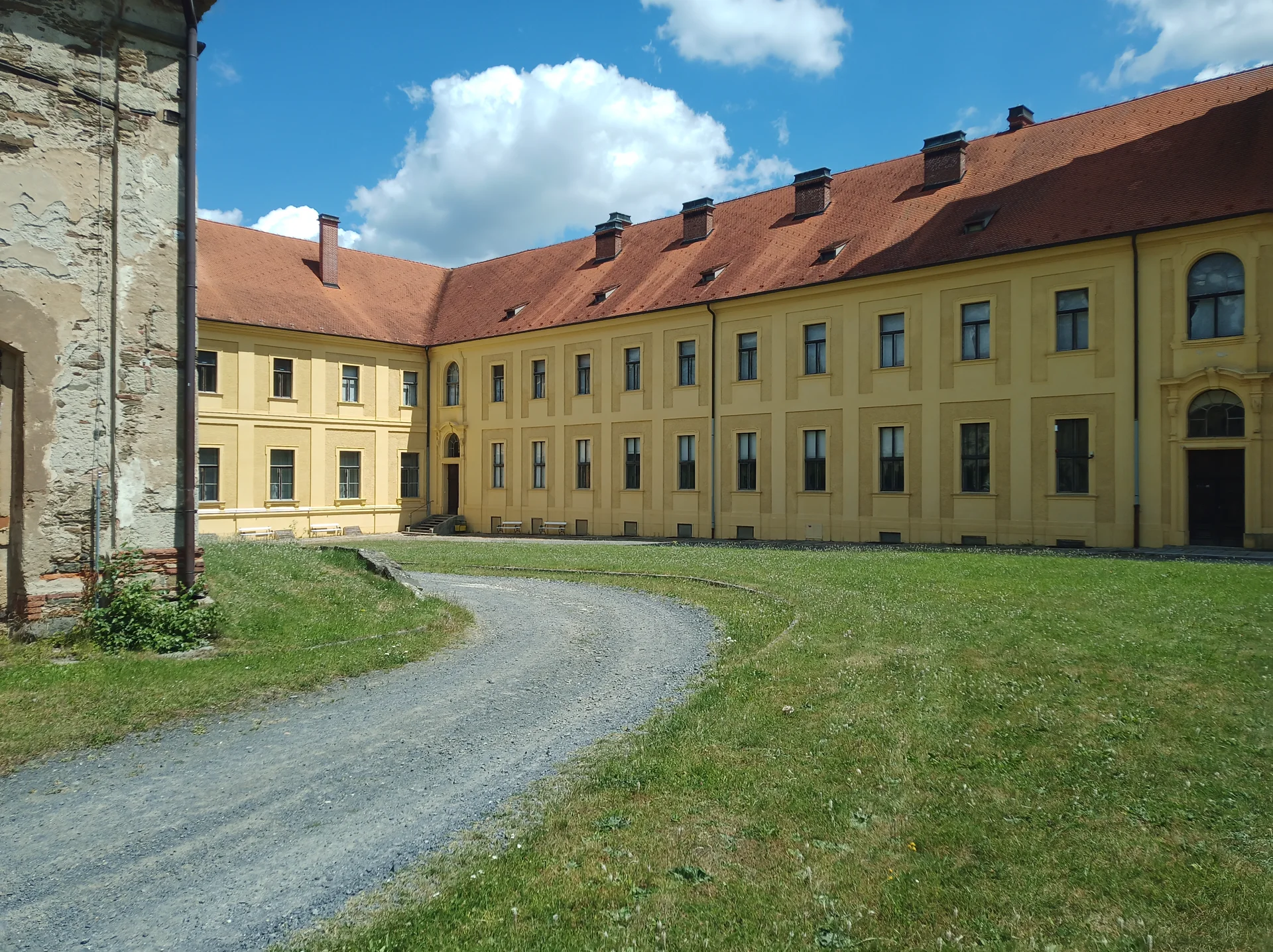Žluté konventní křídlo kláštera s dlouhou řadou oken a cestou v trávníku