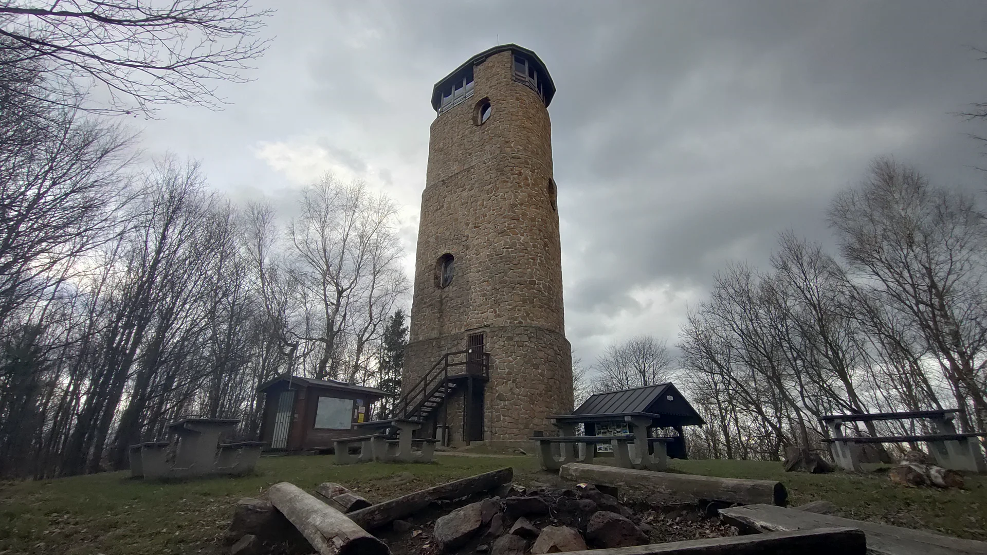 Kamenná rozhledna Brdo v Chřibech, válcová věž s vyhlídkovým ochozem a venkovním schodištěm, kolem bezlisté stromy