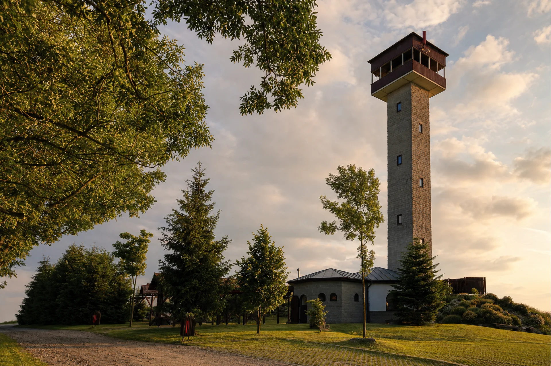 Zděná rozhledna Karasín s krytým ochozem nad areálem, kolem stromy a upravená louka