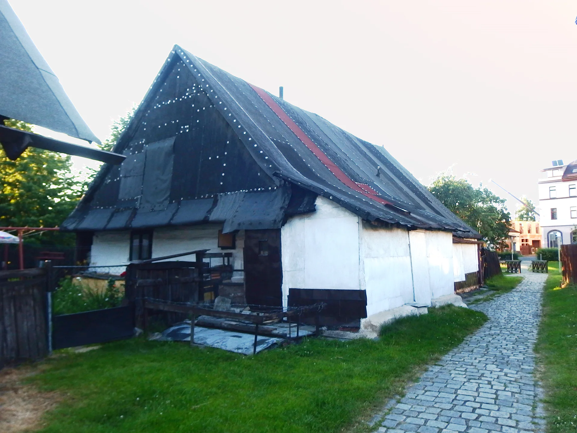 Dřevěný roubený dům s vysokou tmavou střechou u dlážděné uličky v hlineckém Betlémě