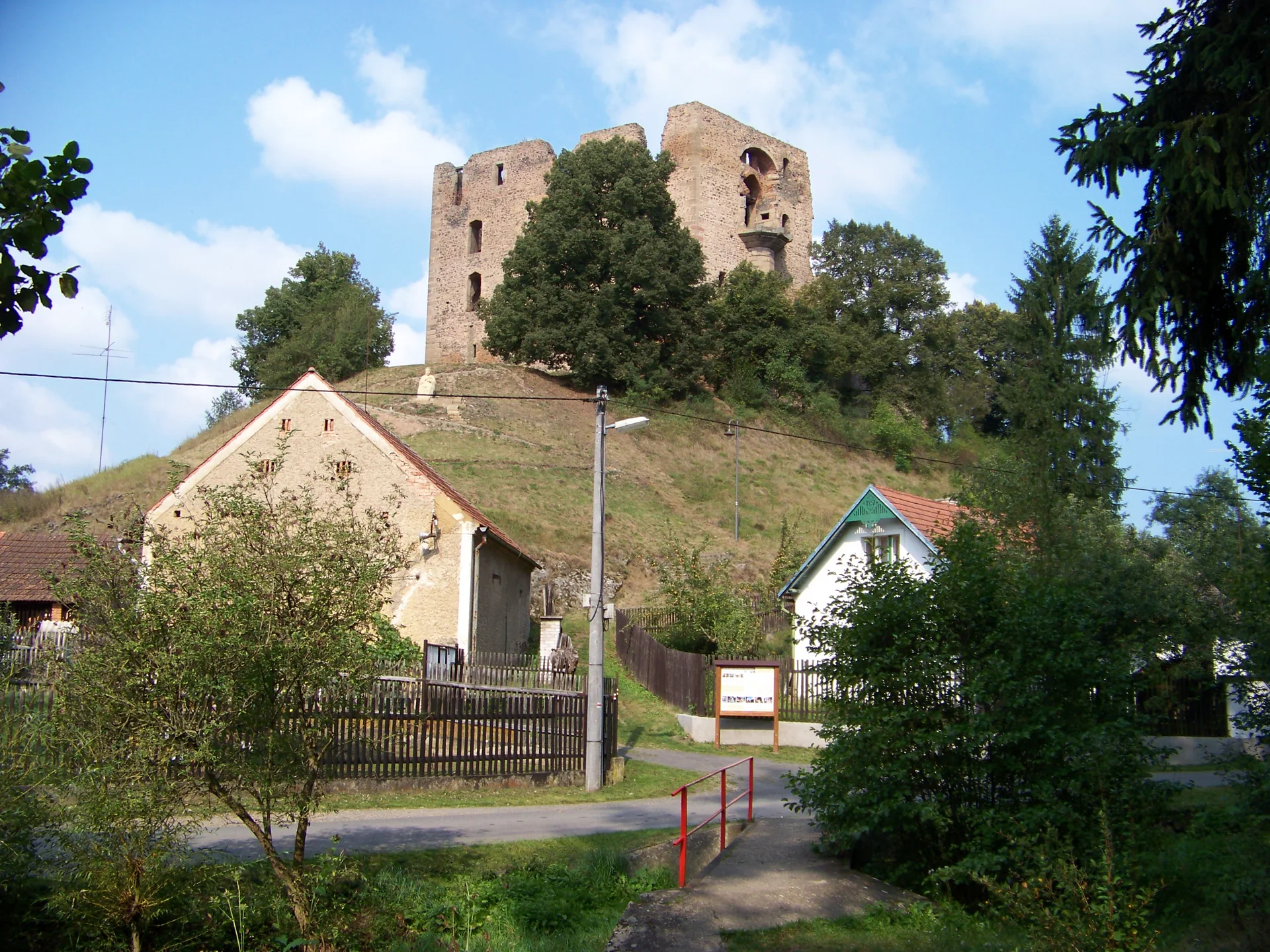 Zřícenina hradu Krakovec na zalesněném ostrohu nad domy vesnice, pohled od jihovýchodu