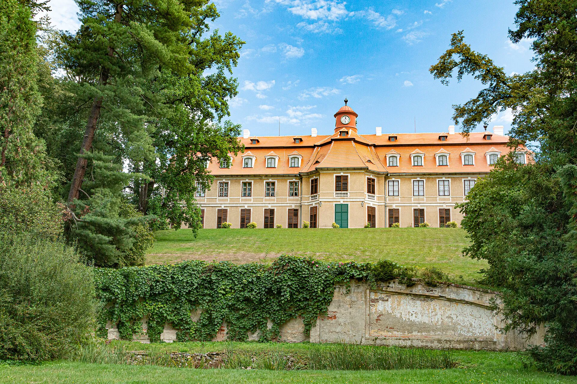 Pozdně barokní zámek prosvítající zelení zámeckého parku