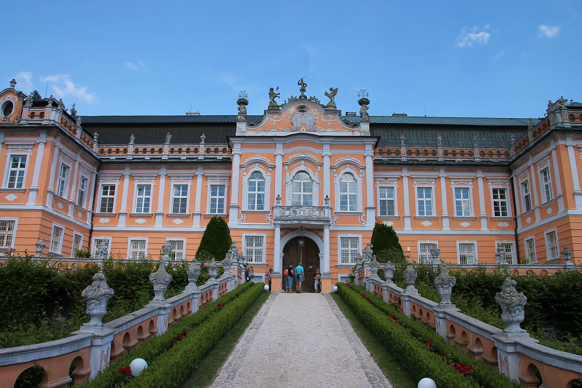 Růžové průčelí rokokového zámku nad cestou lemovanou sochami
