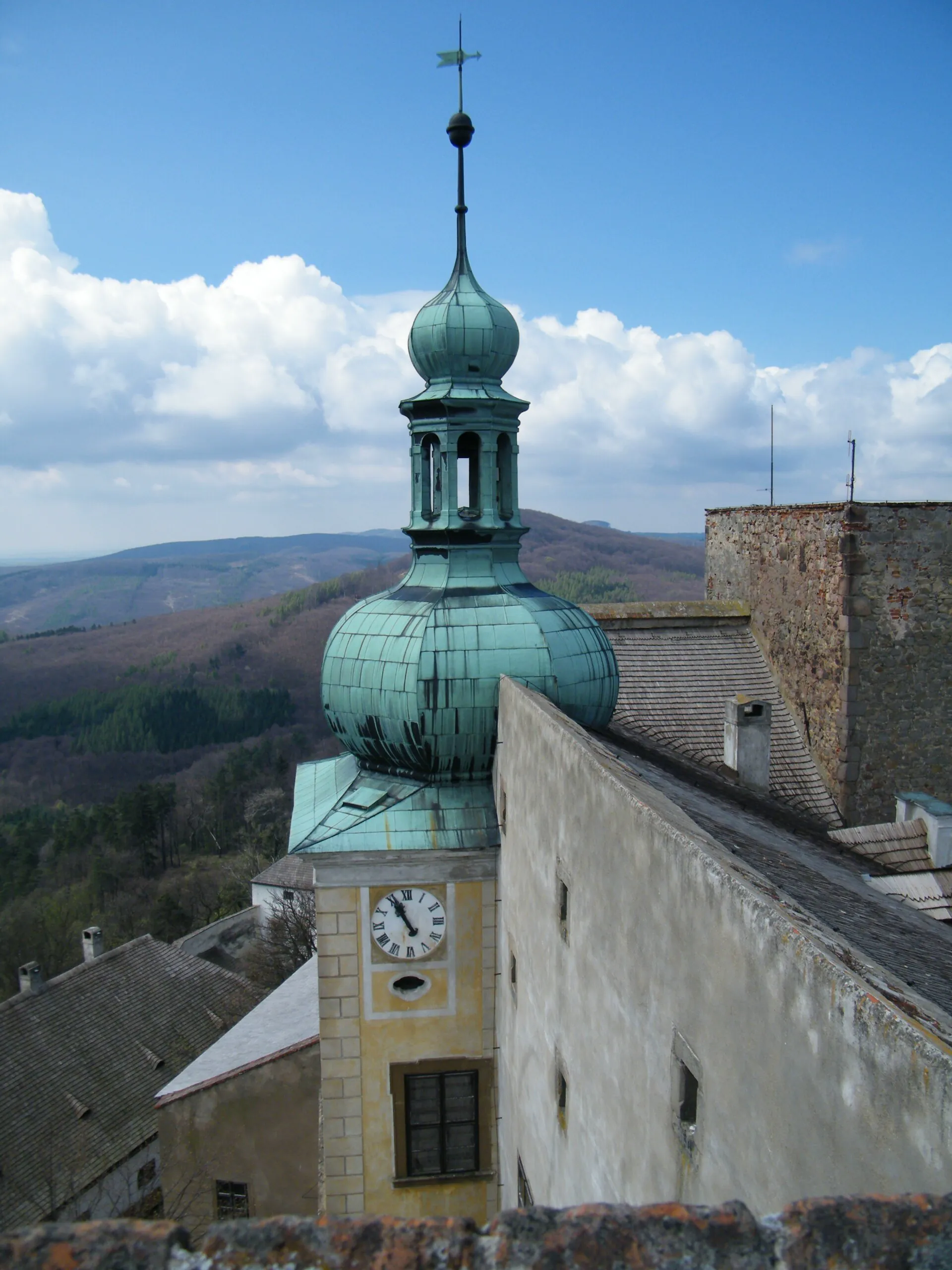 Věž s cibulovou bání a hradními hodinami nad panoramatem Chřibů