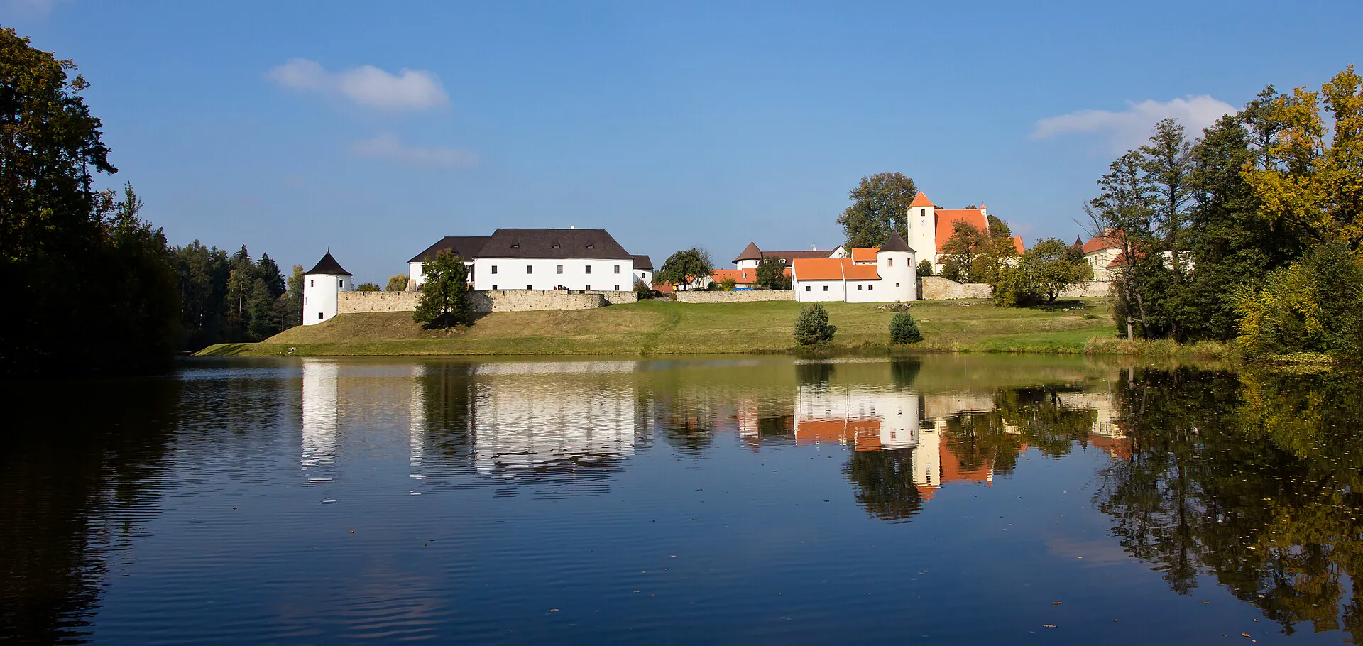 Panorama areálu tvrze nad vodou s odrazem v hladině