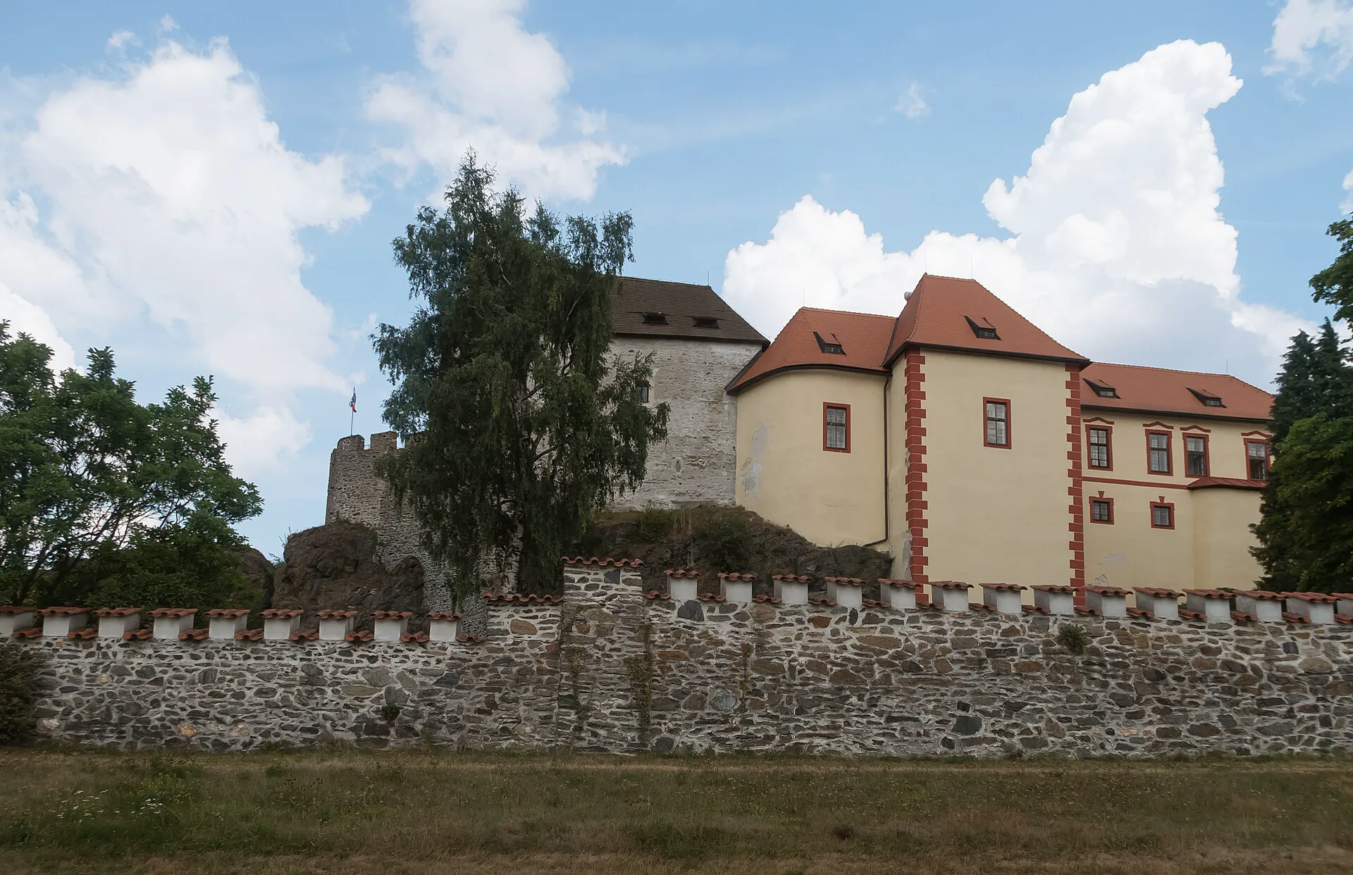 Hrad za kamennou hradbou s cimbuřím a stromy kolem