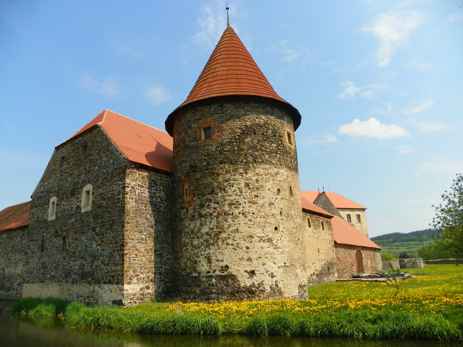 Kulatá bašta hradu s červenou střechou nad vodním příkopem