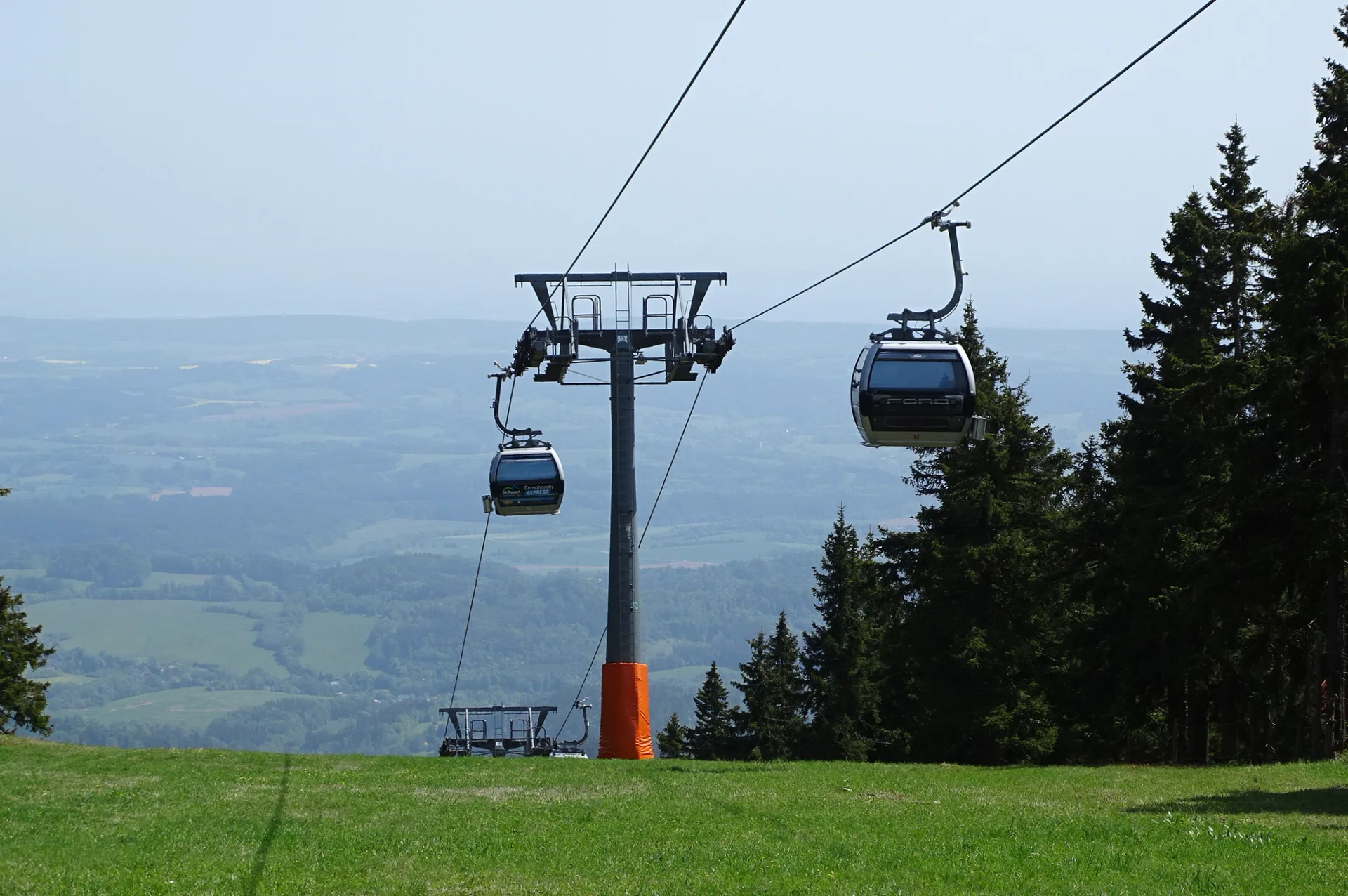 Kabinky lanovky nad loukou s výhledem do podhůří