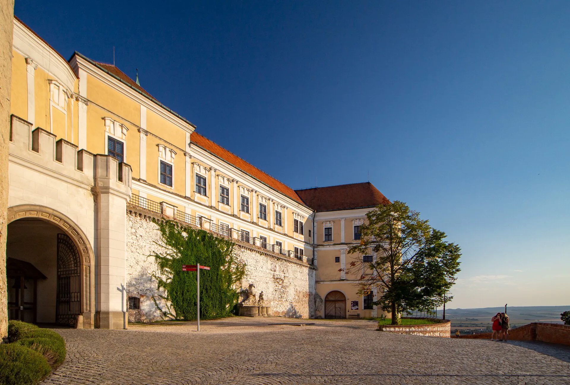 Nádvoří zámku s průjezdem a bránou v podvečerním světle