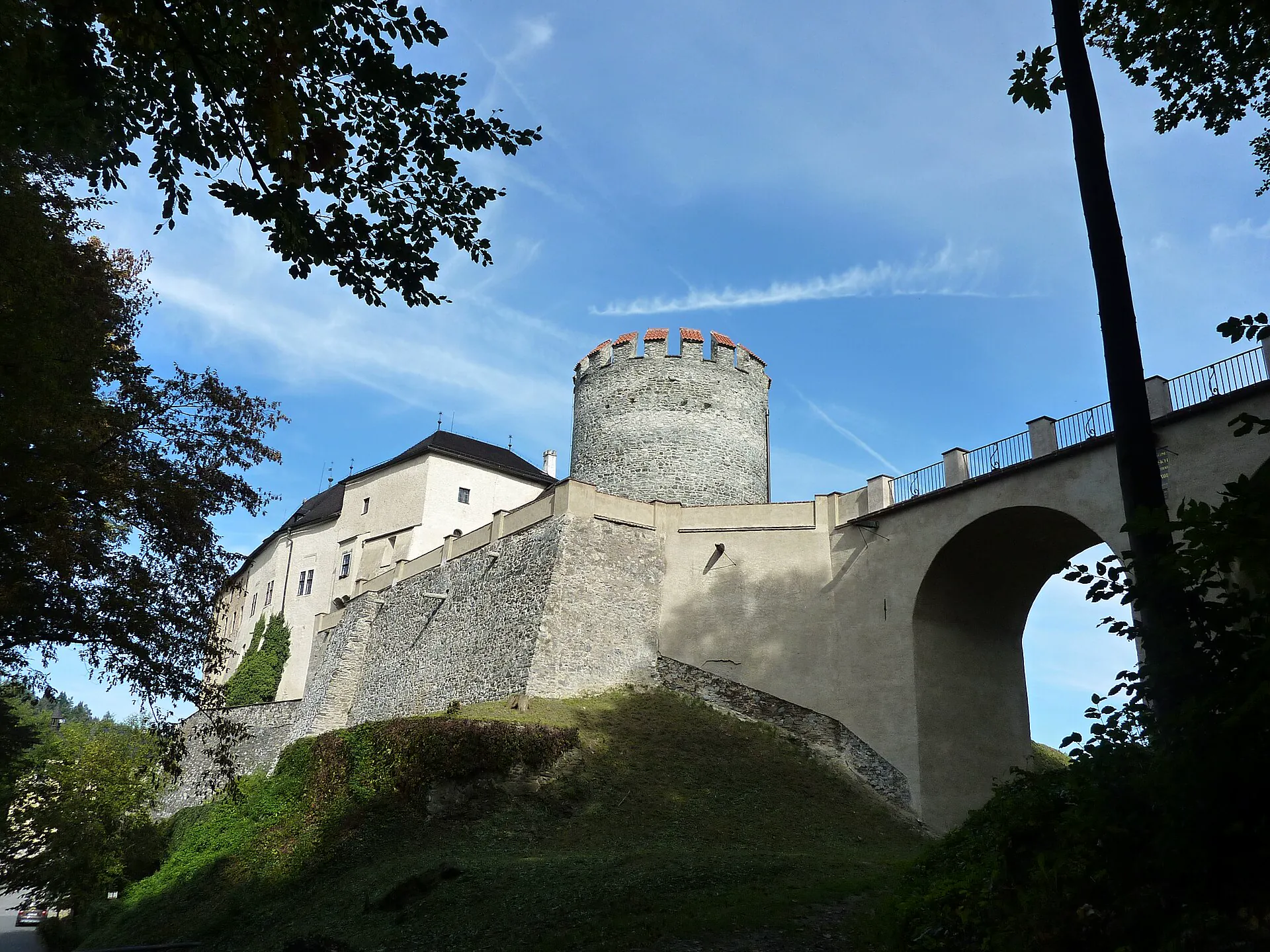 Pohled na hrad zezdola s kulatou věží a klenutým mostem