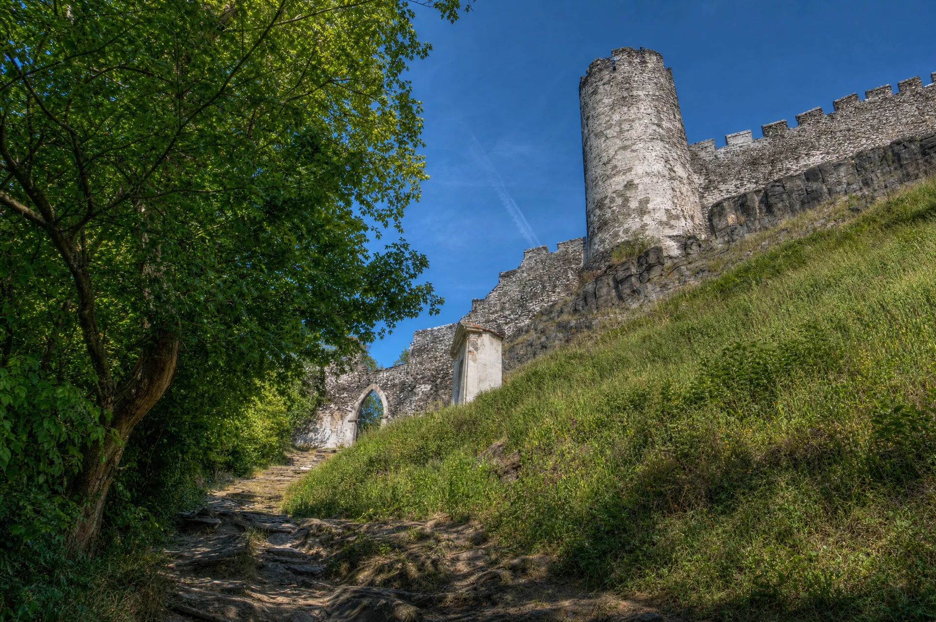 Válcová věž hradu Bezděz s cimbuřím nad kamenitou cestou lemovanou hradbou