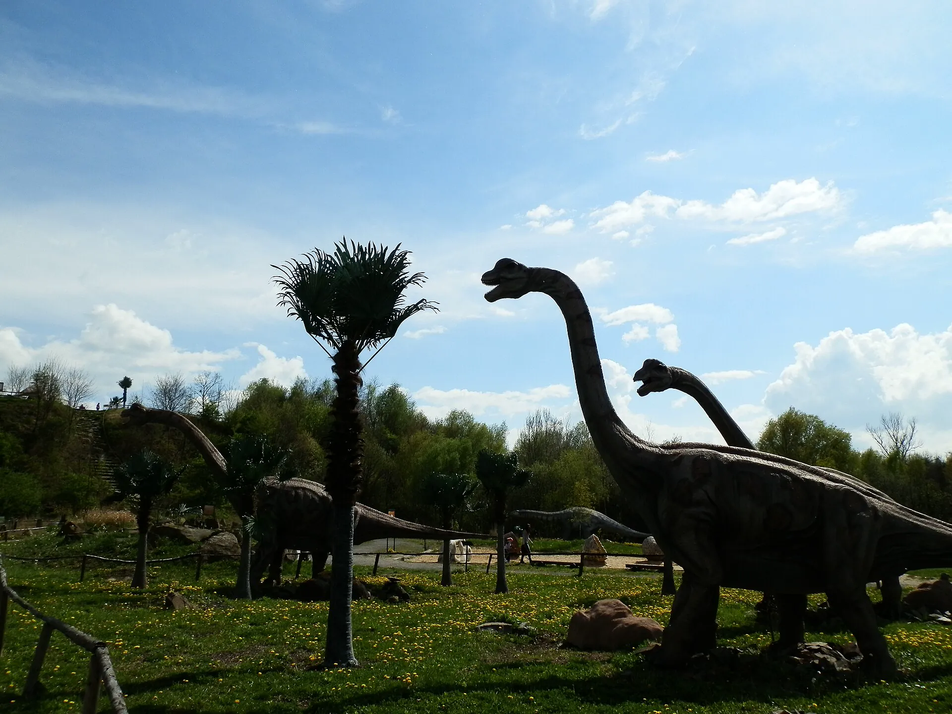 Modely dlouhokrkých dinosaurů v zeleni parku proti obloze